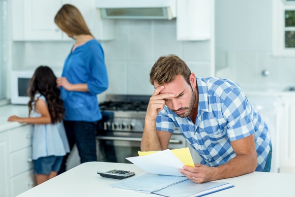 Worried father looking at bills with family in background.