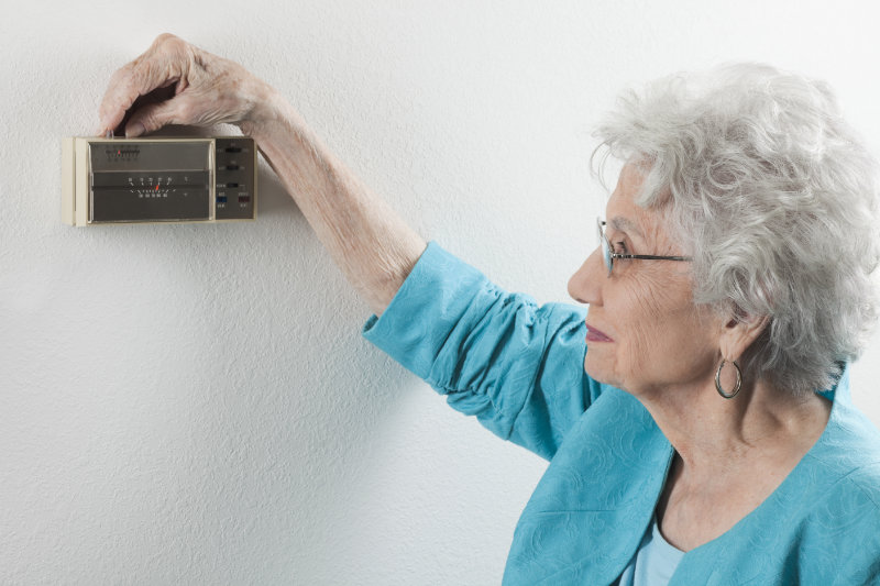 Older woman adjusting the thermostat in her Utica, Kentucky home.