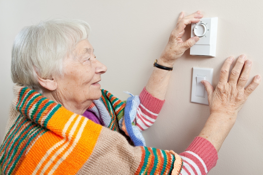 Senior woman staying warm dressing in a blanket and adjusting her thermostat. When Do I Know It’s Time to Buy a New Furnace?