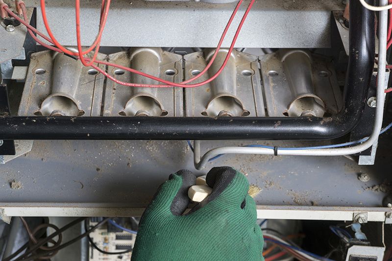 Someone in green gloves working on a furnace. 5 reasons to schedule a fall furnace clean and check.